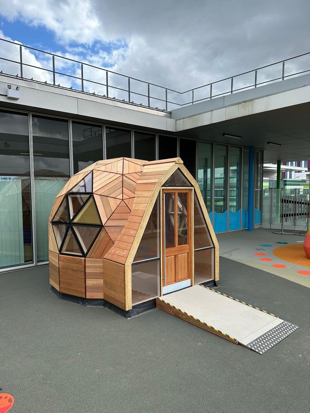 The Huggy Pod, a 3.5m cedar-clad geodesic dome with a full-width accessible ramp on a hospital rooftop play area