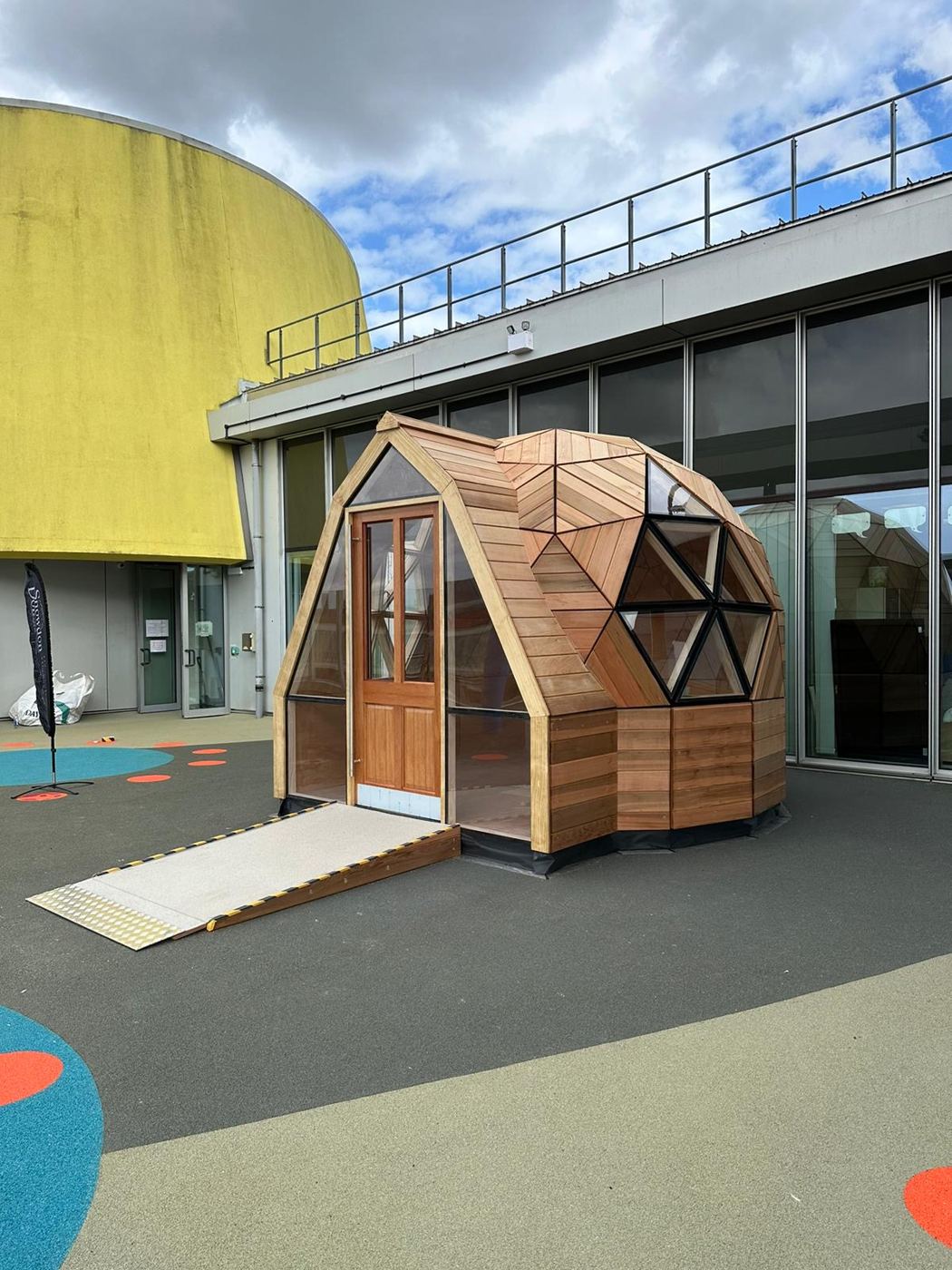 The pod seen across the rooftop play deck, hospital glazing behind